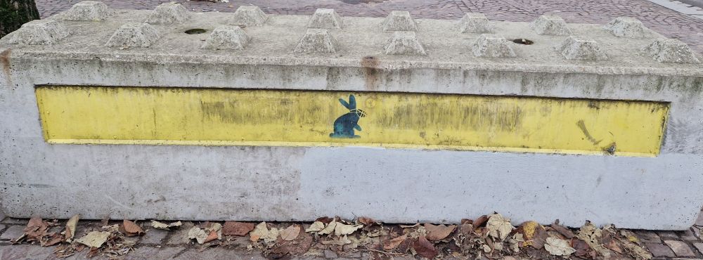Plot horizontal de chantier en béton.
Un lapin avec une muselière est taggué en bleu dessus. 