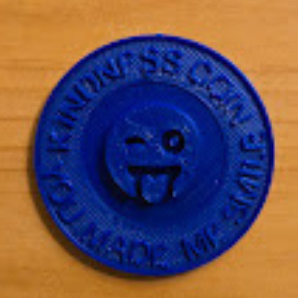 A kindness coin printed in navy filament. It says Kindness Coin you made me smile. The emoji in the middle is of a winking face sticking out its tongue.