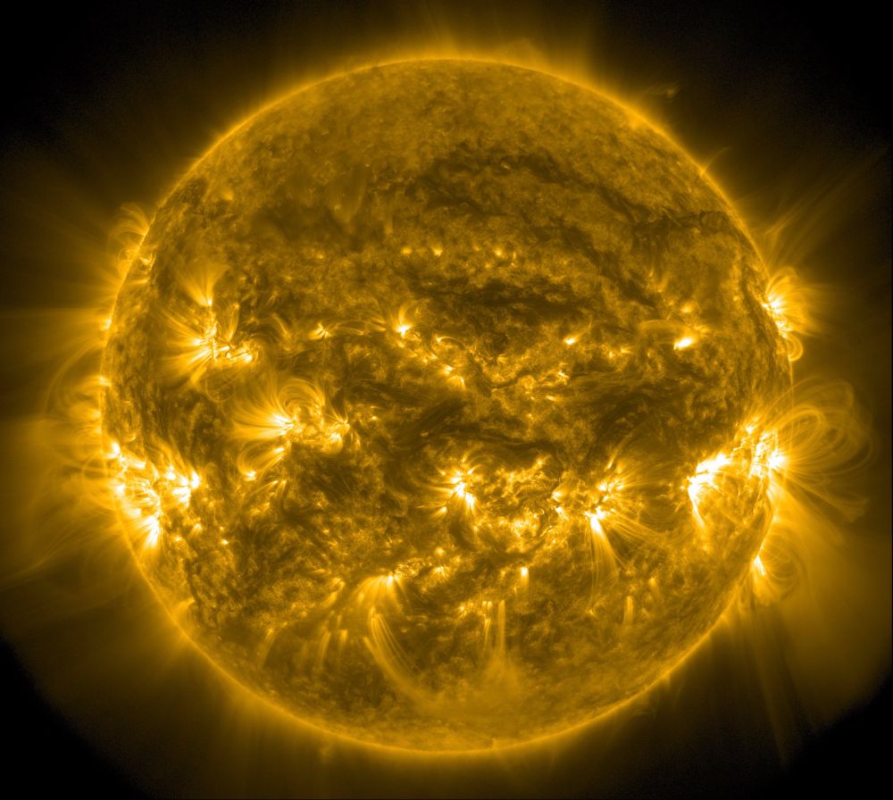 Die ganze erdzugewandte Seite der Sonne in gelber Farbe. Von den Aktiven Regionen, die wie weiße Flecken aussehen, gehen Strahlen weit die Umgebung aus.