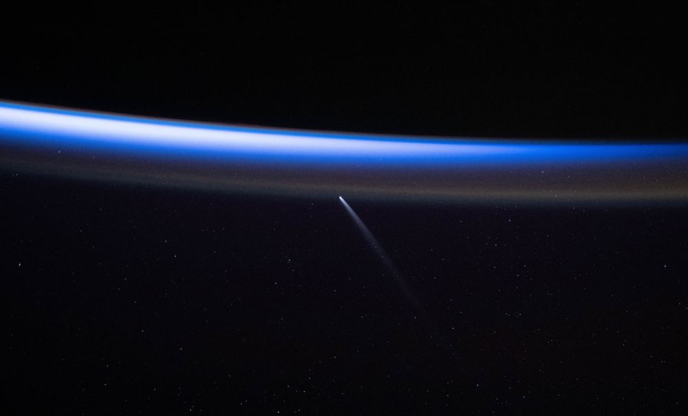 Der Komet als kleiner heller Punkt mit länglichem Schweif unterhalb der Erdatmosphäre, die als dünner hellblauer Streifen leicht gebogen quer durchs Bild verläuft. Dass sich der Komet unterhalb der Erde befindet und der Schweif nach unten zeigt, liegt an der Haltung der Kamera. Zur Erinnerung: Im Weltall gibt es kein Oben oder Unten. Der Astronaut hätte sich oder auch nur die Kamera lediglich drehen müssen und der Komet wäre über dem Horizont der Erde statt darunter.