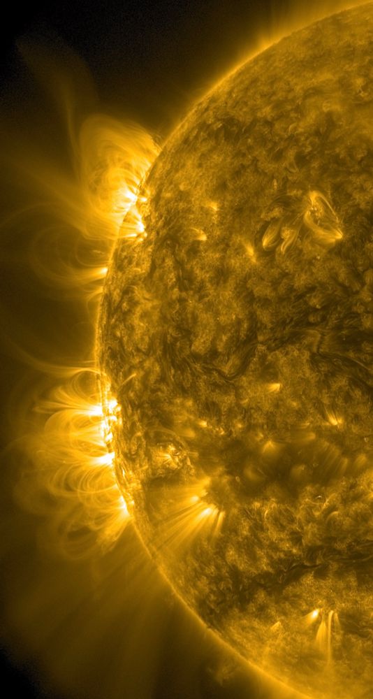 Der linke Teil der erdzugewandten Seite der Sonne in gelber Farbe. Am Rand auf den Zeigerpositionen von ungefähr acht und zehn Uhr zwei gleißend helle Stellen, an denen Strahlen weit ins All reichen. 