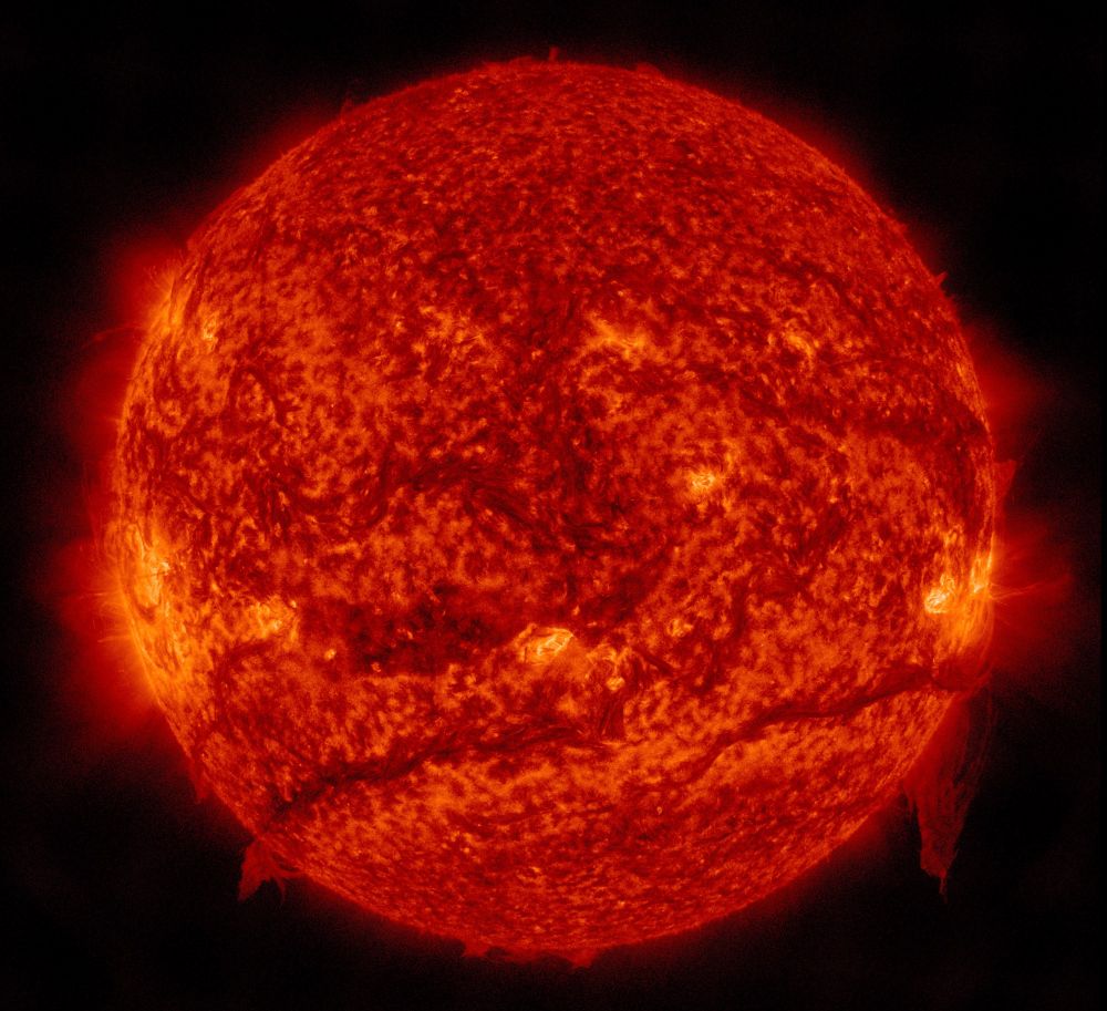 Die erdzugewandte Seite der Sonne in orangeroter Farbe. Zwei auffallend hellere Bereiche links und rechts am Rand mit diffus wirkenden Strahlen, die ins Schwarz des Alls übergehen. Außerdem zwei bis drei dunklere und sehr langgezogene Gebiete, die sich fast über den halben Sonnendurchmesser erstrecken. Das sind sogenannte ruhende Protuberanzen. Im Gegensatz zu eruptiven Protuberanzen, bei denen Sonnenmaterie ins All schießt, verweilen diese Materiestrukturen von den Magnetfeldern der Sonne festgehalten oft wochenlang an derselben Stelle über der Oberfläche. Weil sie weniger heiß sind, sehen sie hier dunkler aus. Irgendwann lösen sie sich und wabern durch die Gegend, bevor sie auf die Oberfläche fallen und verschwinden.