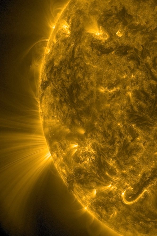 Der linke Rand der erdzugewandten Seite der Sonne in gelber Farbe. Auf der Zeigerposition acht Uhr sieht es wie ein riesiger Fächer aus sehr feinen Lichtstrahlen aus, der von der Sonne ins All reicht und sich dabei mit zunehmender Distanz immer mehr verbreitert.