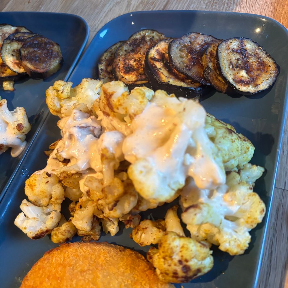 Auf einem blauen Teller: gebratener Blumenkohl mit heller Sauce, dazu gegrillte Aubergine und Cordon Bleu …. alles vegan natürlich. 