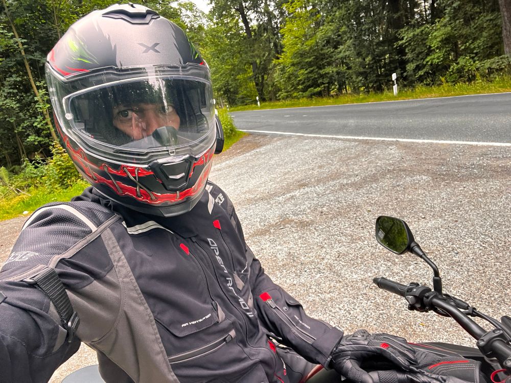 Ich auf einem Motorrad auf einem Waldweg an einer Straße 