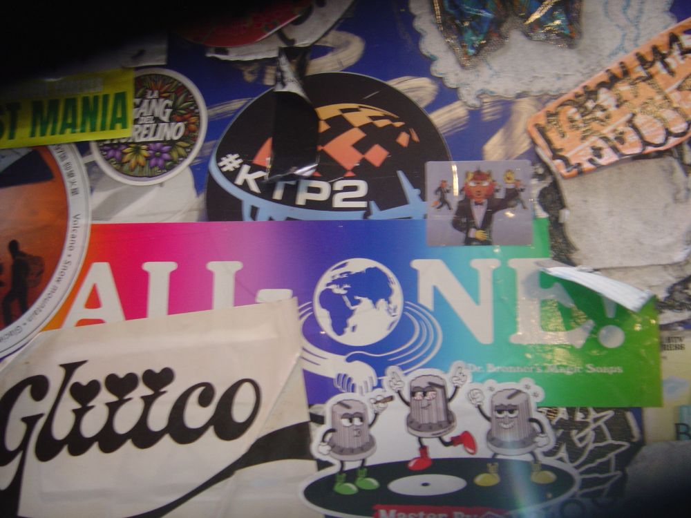 Various stickers on a machine, including a large Dr Bronner's bumper sticker and a small furry sticker.
