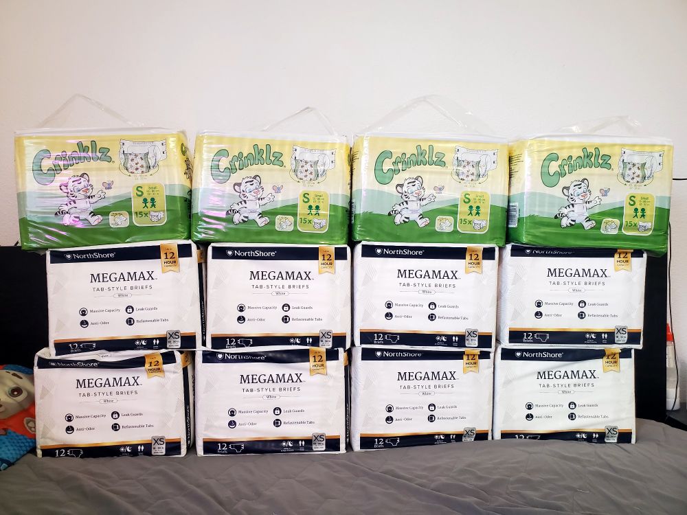 A wall made out of packs of diapers stacked on top of one another. 8 bags of white XS Megamax, 4 bags of S Crinklz.