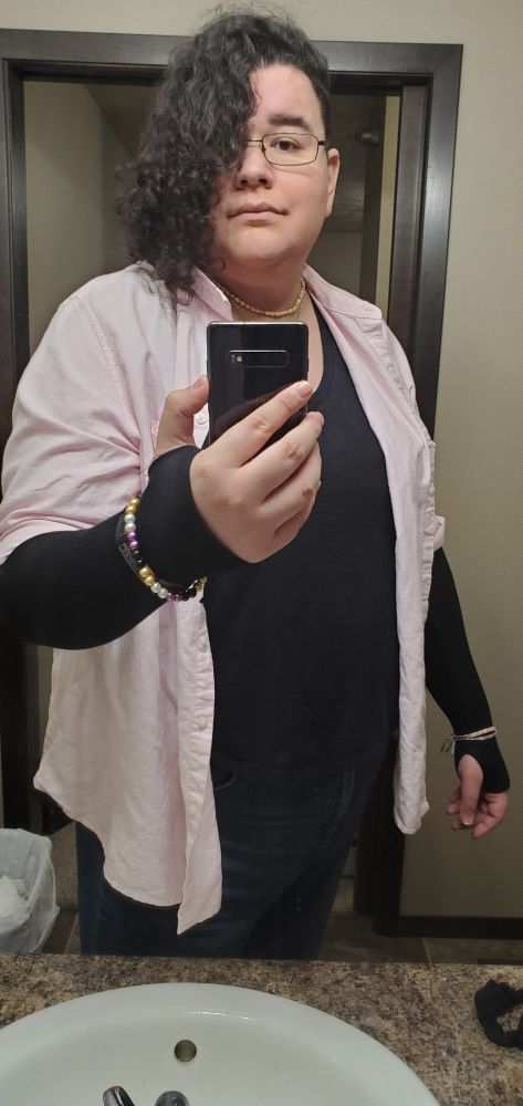 A trans woman in a pink overshirt taking a selfie. 