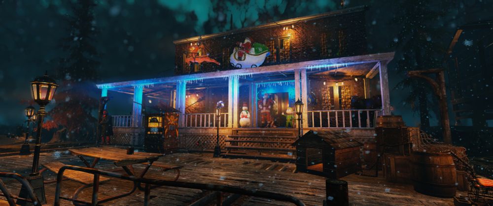 A screenshot from the video game Fallout 76, it is nighttime and snow is falling, the sky is a dusky blue. In the centre of the image we see a house with a long and wide porch, blue Christmas lights that look like icicles hanging from the eaves. I'm the foreground we see wooden decking with a bench and an old gas light street lamp as well as a dog kennel with some assorted clutter and barrels to the right. The house has a snowman and elf at the top of a small set of steps up towards the front door area, I person dressed as Santa clause can be seen in the doorway. There is also a large Santa on a sleigh decoration with a single reindeer on the roof of the porch. 
