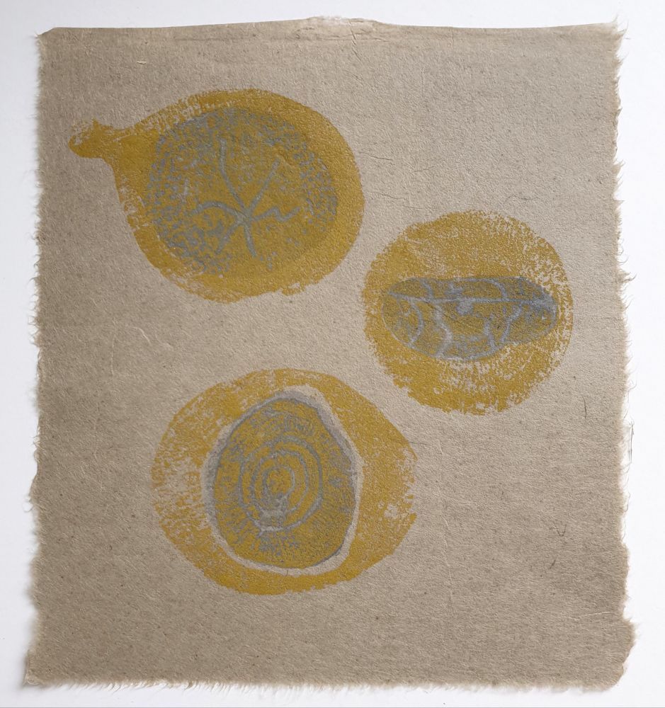 3 yellow woodcuts of pebbles on sandy coloured Japanese paper, the pebbles have been painted over with bluegrey watercolour. 