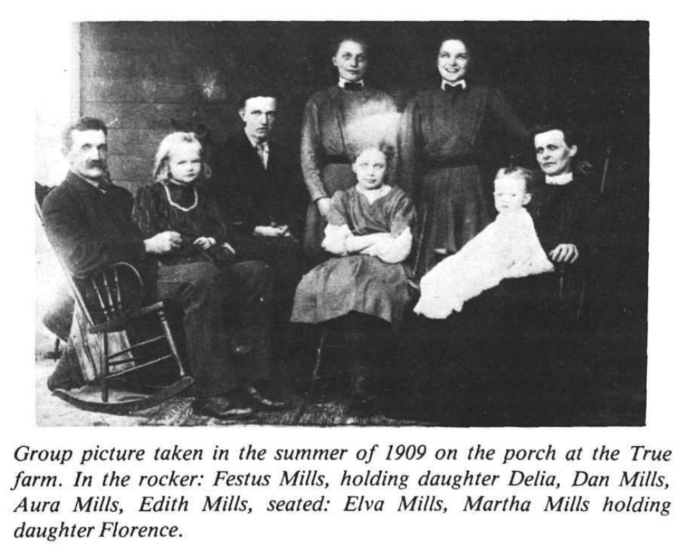 Festus Mills and his family pose for a group picture on a porch in 1909. Festus is seated in a rocking chair, holding his daughter Delia.