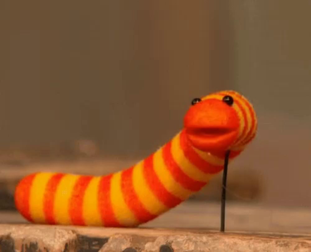 a stuffed worm with a yellow and orange stripped body is sticking out of a hole in a wall