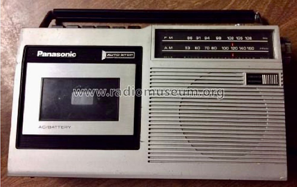  The image shows a Panasonic portable radio cassette player. On the left side, there is a cassette compartment with a transparent window, allowing visibility of the cassette inside. Above the cassette compartment, the brand name "Panasonic" is displayed prominently, along with the label "AUTO STOP." Below the cassette compartment, the text "AC/BATTERY" is visible, indicating the power options for the device.

To the right of the cassette compartment is the radio tuner section. This section includes a frequency display for both FM and AM bands. The FM band ranges from 88 to 108 MHz, while the AM band ranges from 53 to 160 kHz. A red indicator is present on the frequency display, likely used to show the current tuning position.

Further to the right is the speaker area, which is characterized by horizontal lines that likely serve as a grille. Adjacent to the speaker, on the far right, is a control knob, possibly for volume or tuning adjustments. The top of the device features a handle for portability. The website "www.radiomuseum.org" is overlaid on the image, indicating the source of the photograph.


