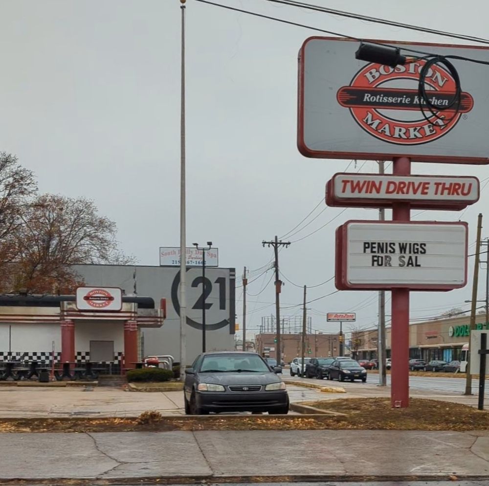 A picture of an abandoned Boston Market in an old Checker's drive-thru. The sign reads: penis wigs for sal