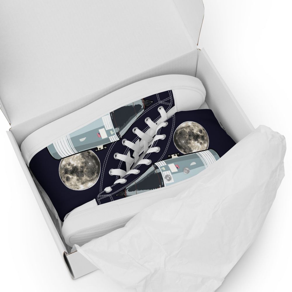 A qhite shoebox on white background, containing a pair of high-top trainers made of dark blue canvass, featuring the moon and the Apollo Command & Service Module on the side panels.