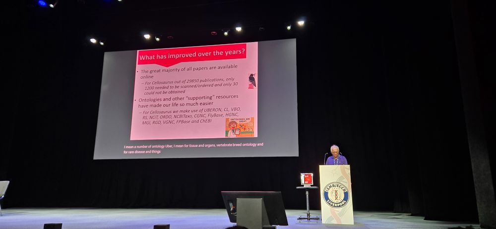 Amos Bairoch stands at a podium in front of presentation slides at ISMB2025