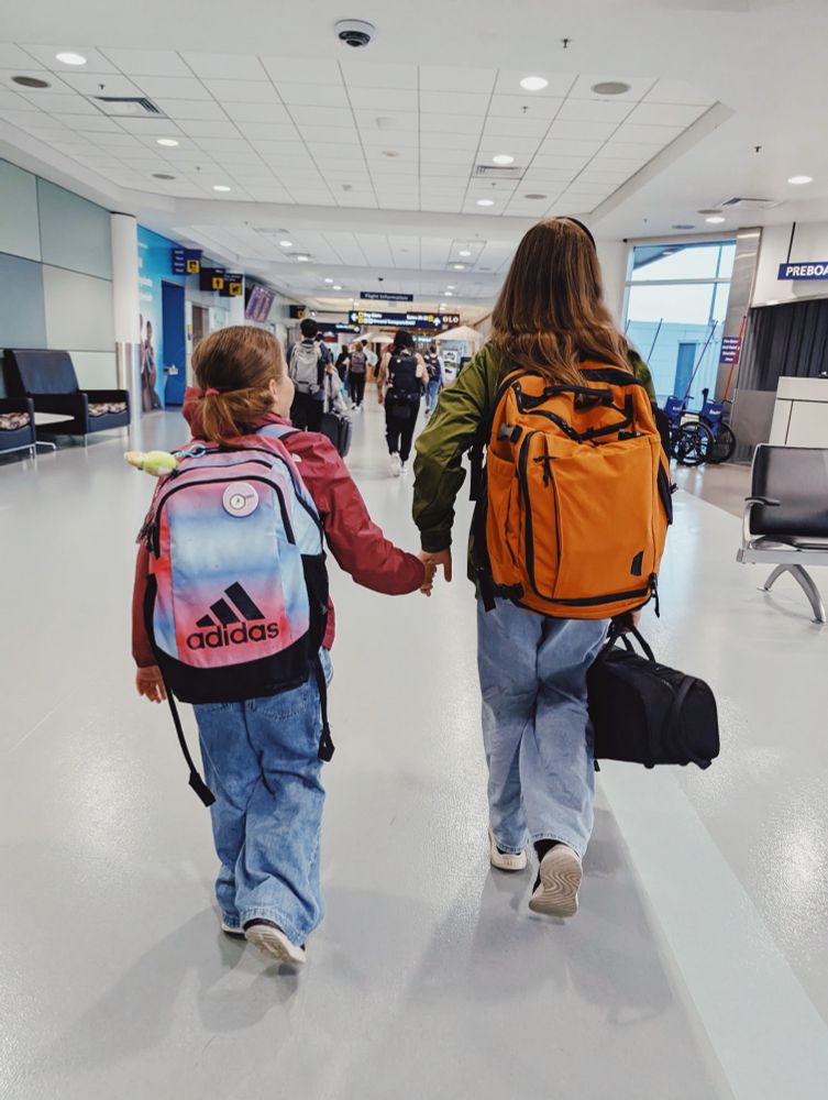 Two sisters with backpacks walking hand in hand in the airport 