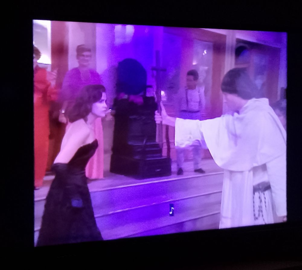 Cena da novela Hilda Furacão. Os personagens Hilda e Frei Maltus estão se encarando. Maltus brande uma cruz em frete a Hilda.