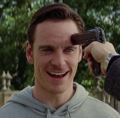 Erik smiling oddly wild while his unofficial husband Charles holds a gun to his head