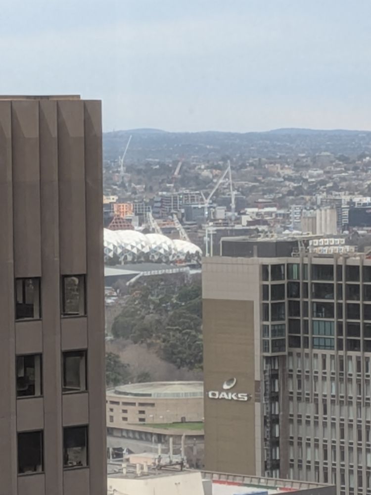A picture of Melbourne rectangular stadium in the distance between Melbourne's CBD tall buildings 