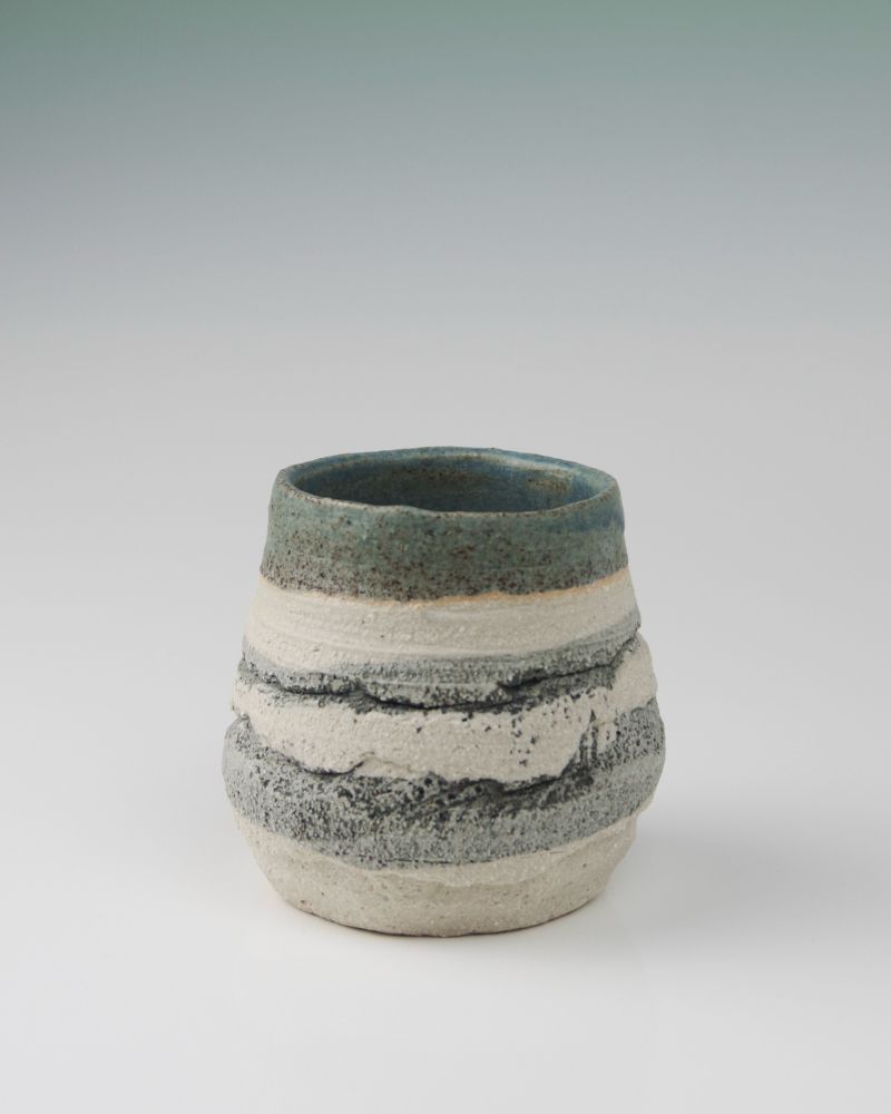 A rough textured pot on a clean white background. The pot is decorated with black oxide across the texture - contrasting the white bare clay. It is glazed inside with a green blue glaze.