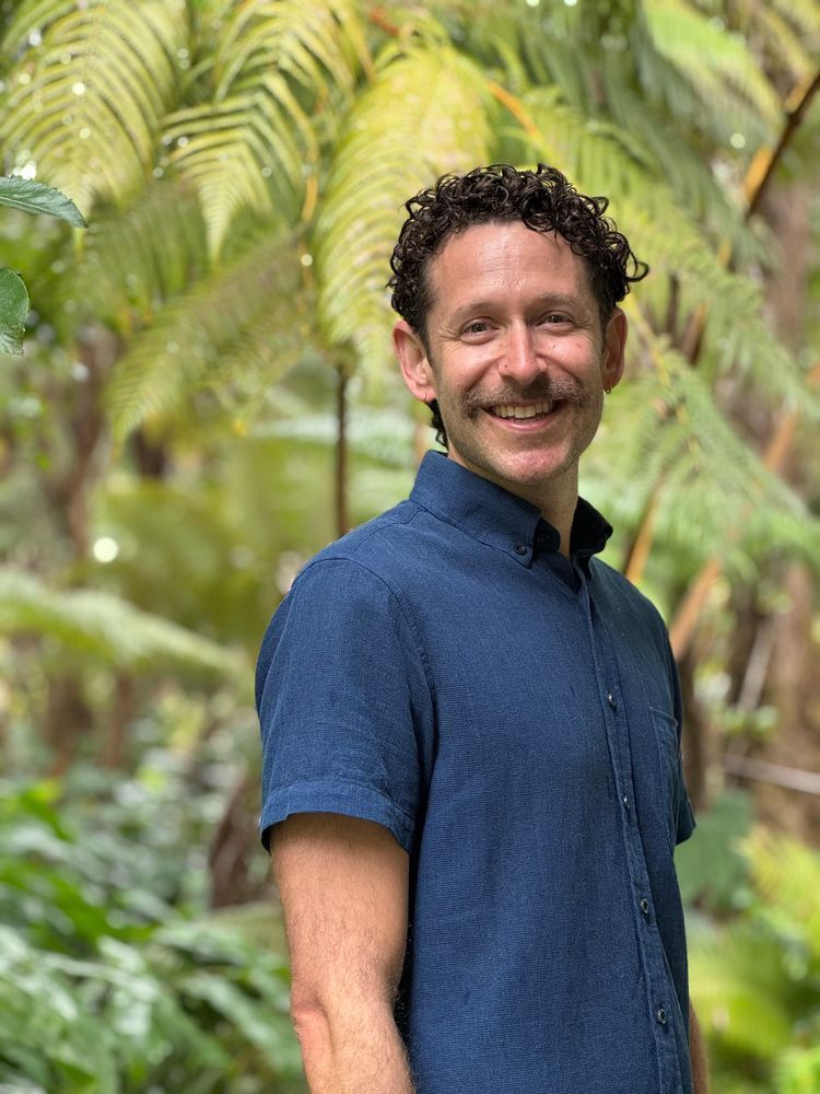 A picture of Dr. David Green wearing a blue shirt in front of some green foliage.