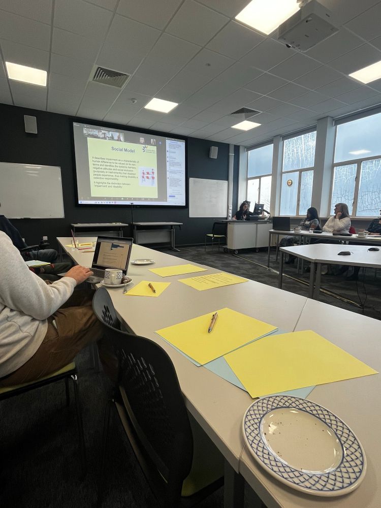 Photo of a meeting room displaying a slide about the social model of disability