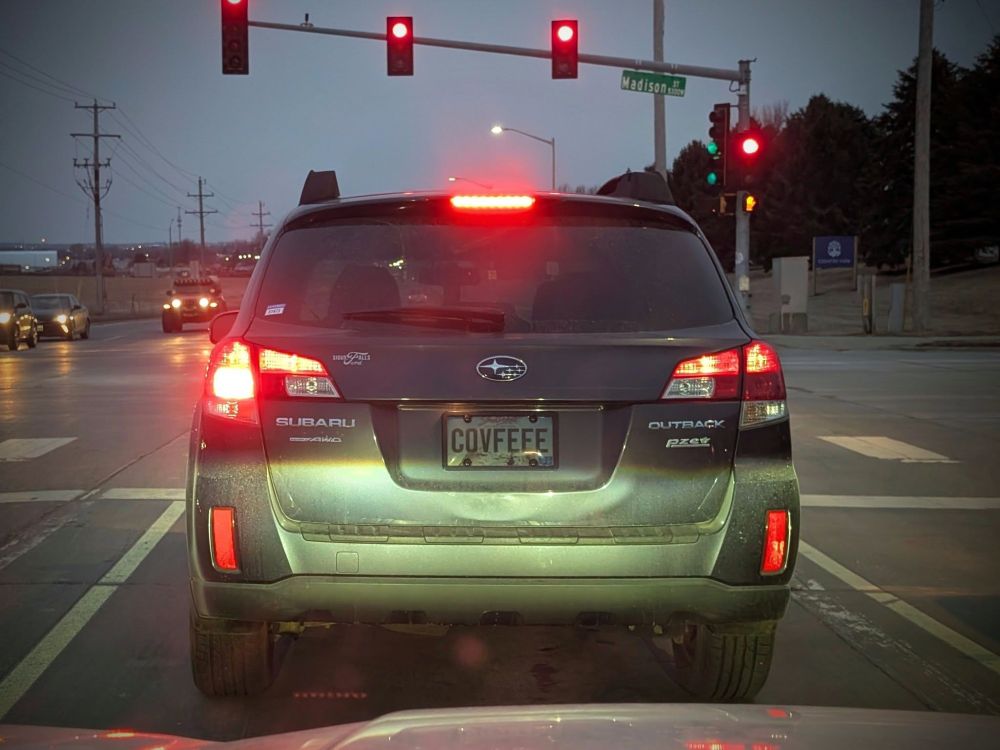 A Subaru Outback stopped at the light as seen from the car behind it. The custom license plate reads "COVFEFE".