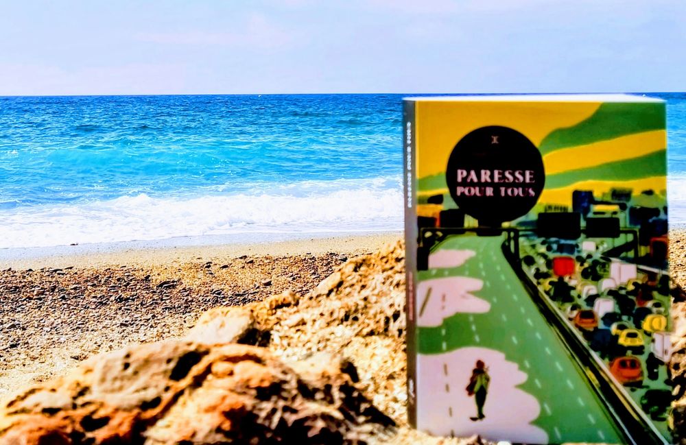 Livre "Paresse pour tous" devant la Méditerranée, les rochers et le ciel bleu 