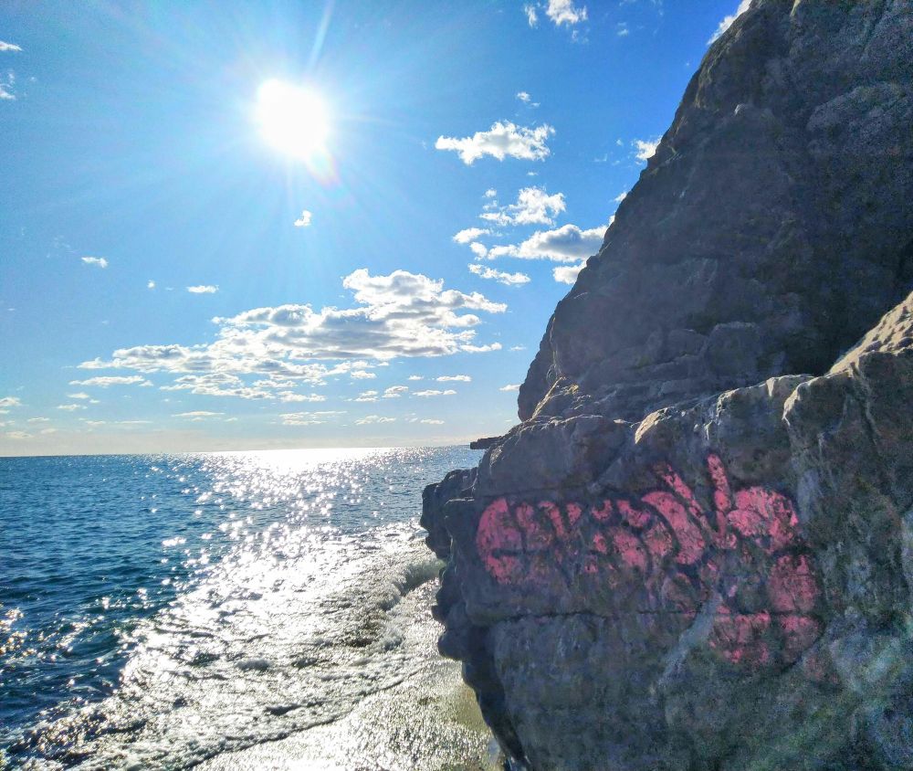 Soleil lumineux sur Méditerranée et rocher avec graffiti rose sur la droite 