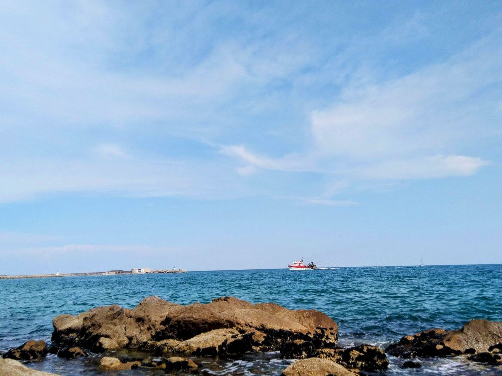 Rocher et Méditerranée, un chalutier rouge à l'horizon rentrant au port à Sète 