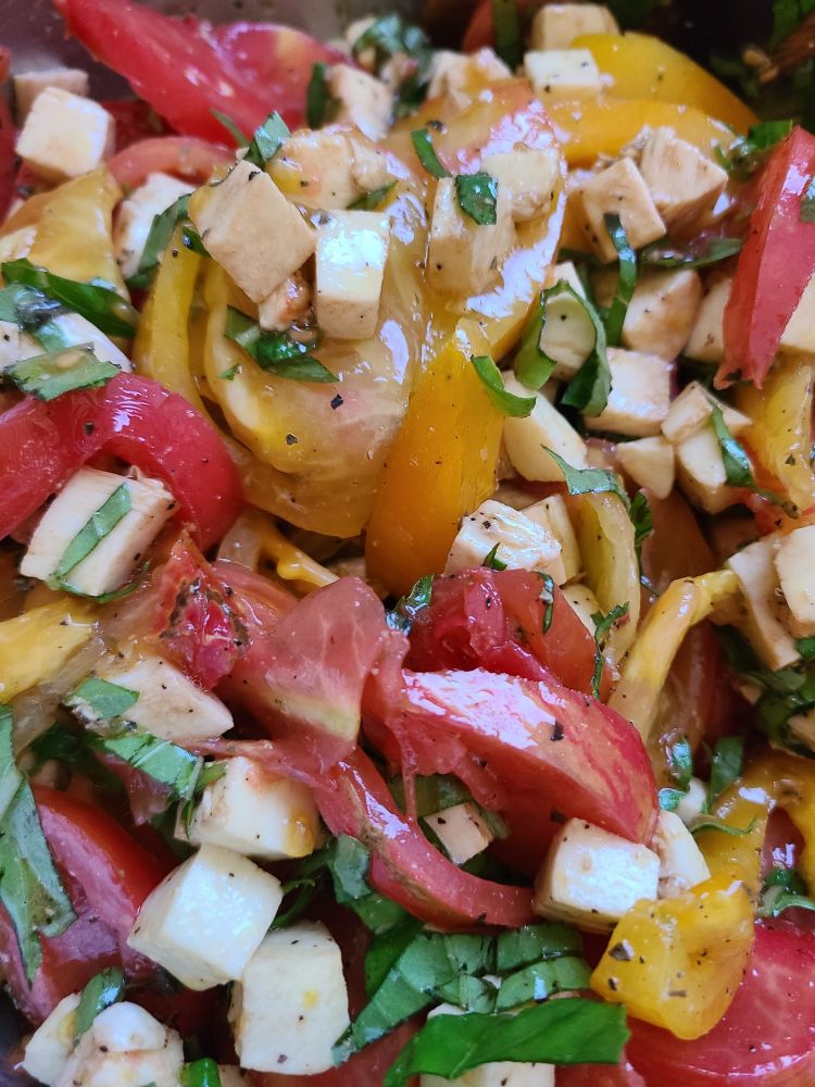 Red tomatoes, yellow tomatoes, stripey red and yellow tomatoes all piled in a bowl with chopped basil and cubed fresh mozzarella