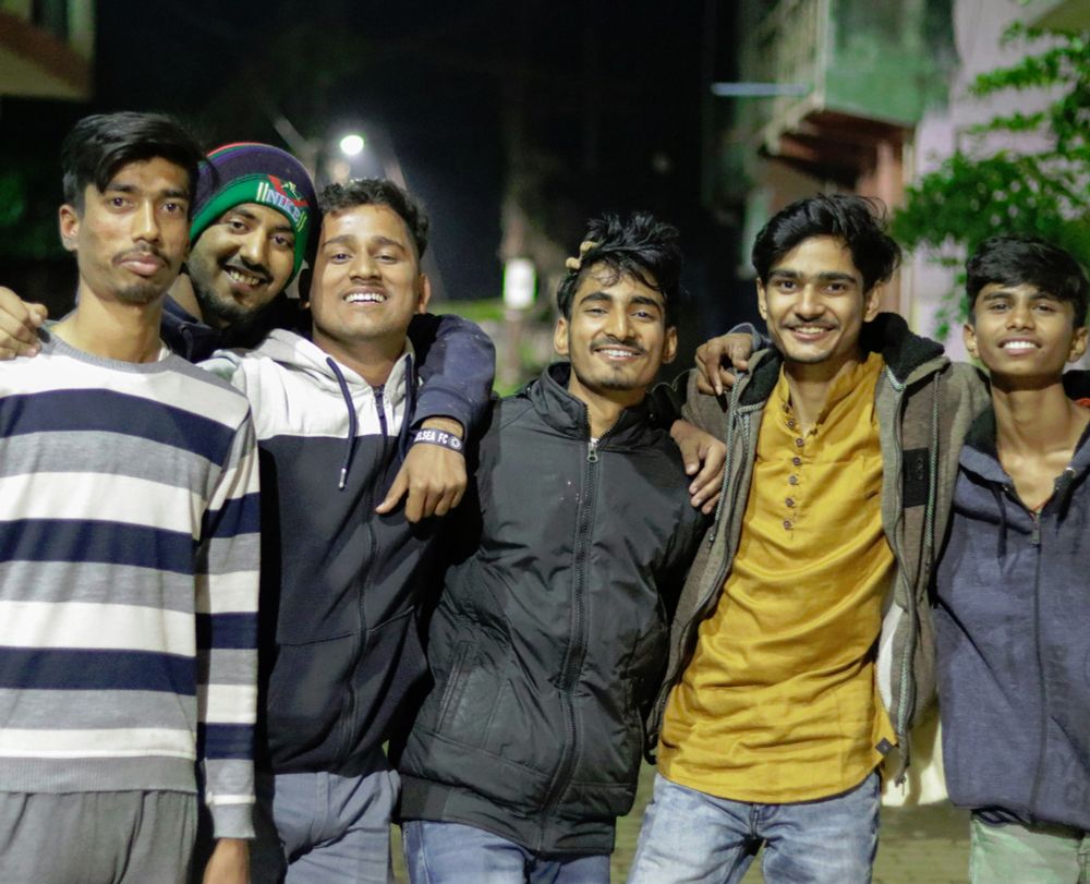 A group of youth in India at night with arms around each other's shoulders, smiling for the camera. Image credit: Sanket Mishra, Unsplash.