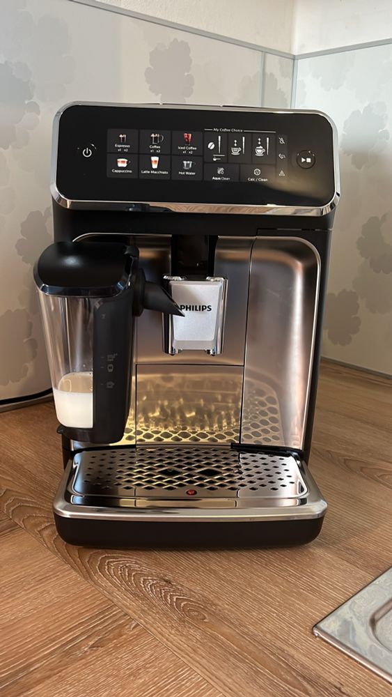 Philips Kaffeevollautomat auf einer Holzstruktur-Arbeitsplatte, vor weißem Spritzschutz mit grauen Blumen.