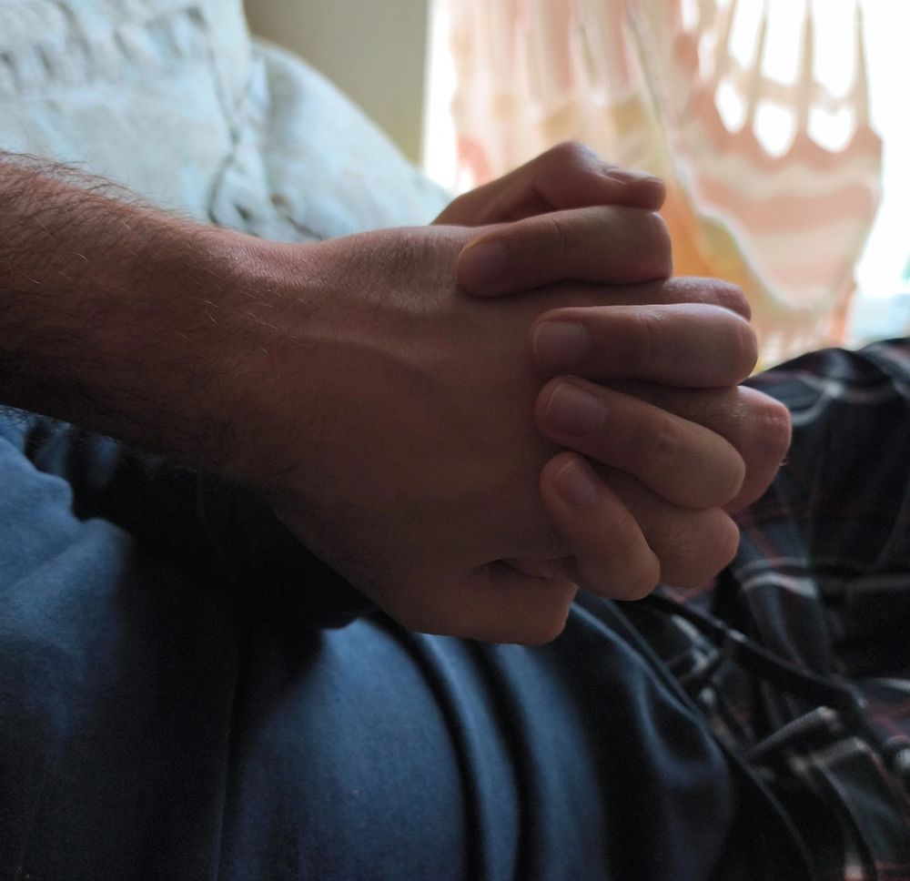 Enfoque de duas mãos de pessoas diferentes entrelaçadas, apoiadas sobre o tronco de uma delas.