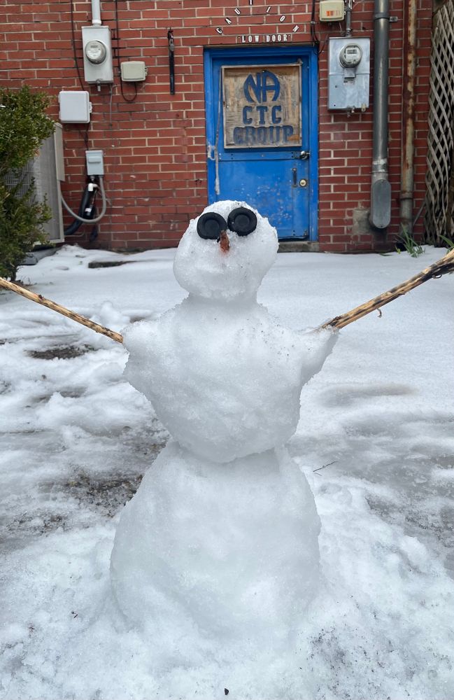 A little snow man has been made with snow all around it on the ground. 