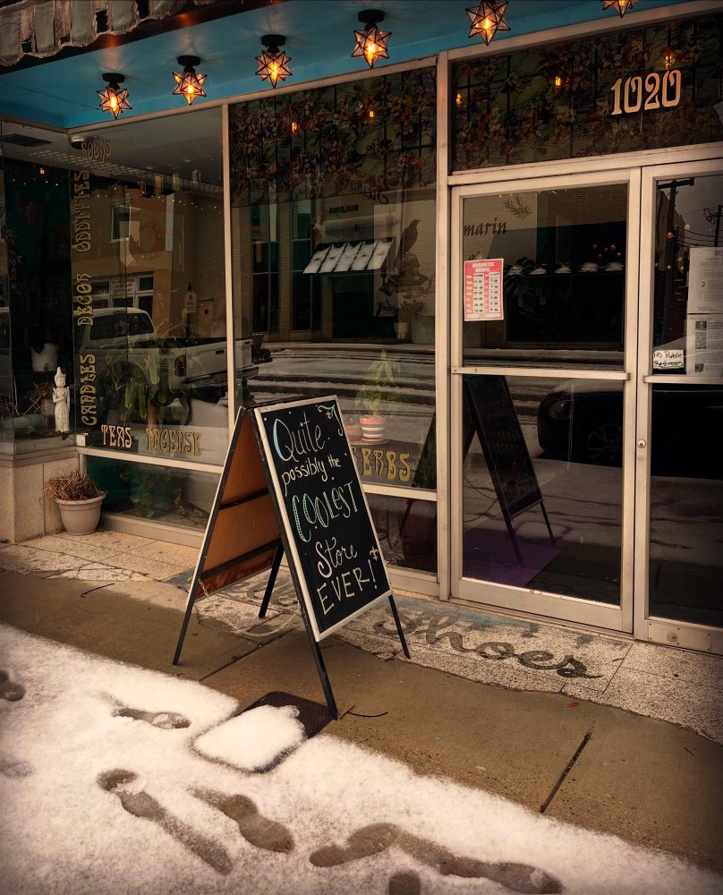 Store front is shown with snow on the sidewalk in front of it. 