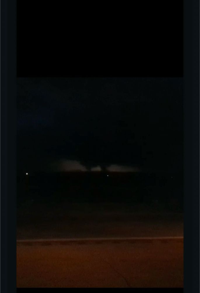 Twin vortex tornado are lit up by lightning across the open plains at night, captured a few miles away