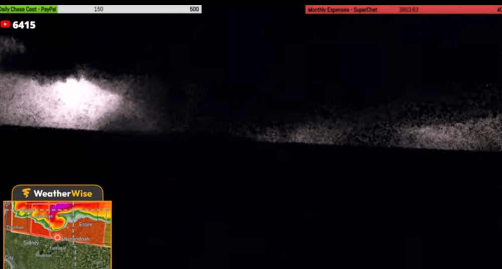 A massive wedge tornado is captured on a livestream at night, lit by a lightning flash. The quality is poor and grainy but the tornado is so big it still looks apparent and terrifying