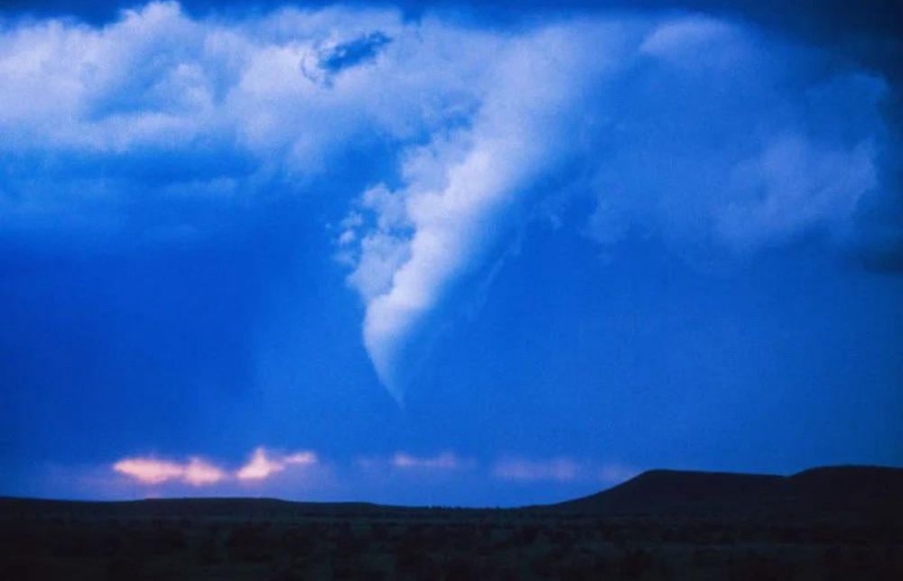 A unique and thick funnel cloud breaks through a layer of clouds on the Colorado plains, the cool blue tones of twilight turning the tornado and its surroundings blue, technical term for it would be “blue hour” in photographer speak