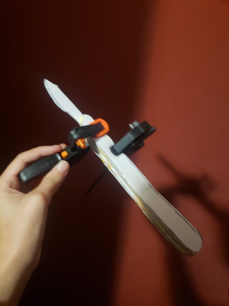 Some clamps holding together pieces of craft foam cut into the design of a scalpel.