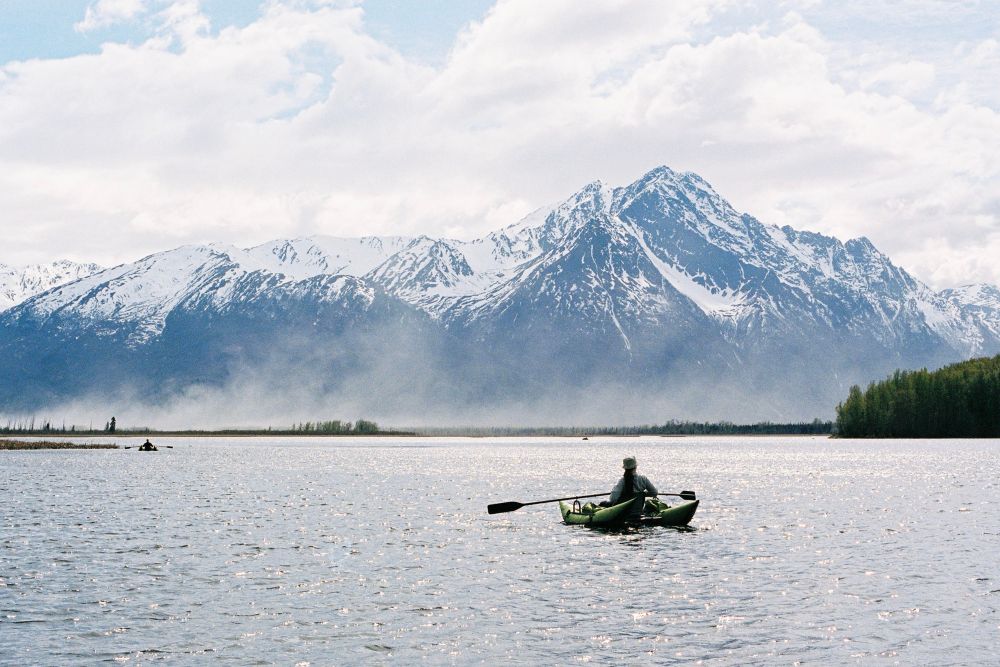 A researcher in a boat out on a lake with mountains looming behind 