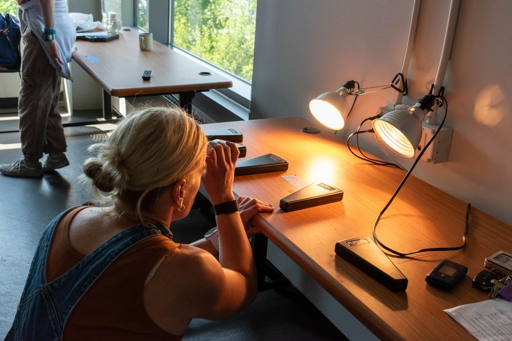 A woman in overalls uses a handheld spectroscope to examine wavelengths from two different types of lightbulbs. Credit: MNSG/A. Shie