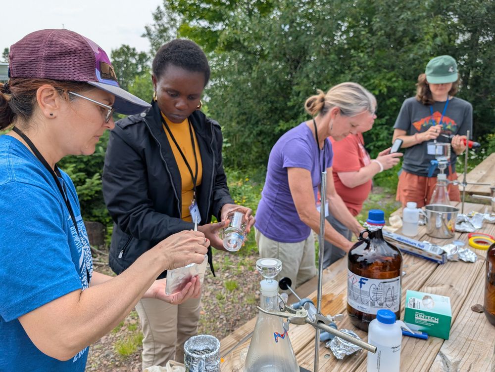 Educators stand in a row preparing a science equipment in front of a bench with scientific equipment on top. Credit: MNSG.
