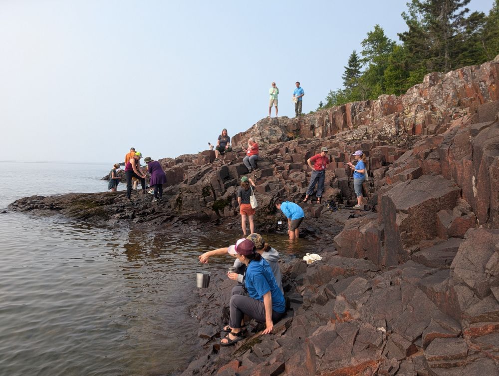 Educators in pairs look at pails of water from along a rocky shoreline of Lake Superior. Credit: MNSG.
