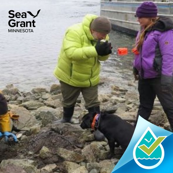 Three people wearing winter jackets on a rocky shoreline with a black dog. Image credit: NOAA.