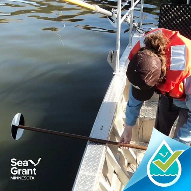 A woman wearing a life jacket on a boat holds a stick with a secchi disk at the end of it. Credit: USFWS.