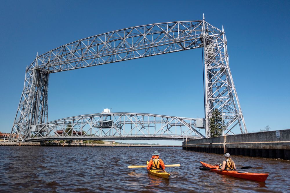Two kayakers paddling in front of the Duluth Aerial Lift Bridge on a clear day. Credit: UMPR.
