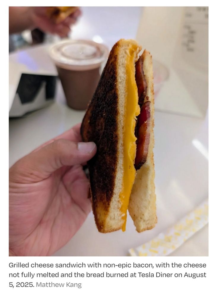 A picture of an epic bacon sandwich at the Tesla Diner. The image shows a grilled cheese sandwich with bacon and a slice of unmelted (as in, it looks like you just took it out of the fridge, it looks *cold*) American Cheese, as well as bread that's burnt on the outside and still lily white on the inside.

A caption on the image says the following:

"Grilled cheese sandwich with non-epic bacon, with the cheese not fully melted, and the bread burned at Tesla Diner on August 5, 2025. Matthew Kang." 