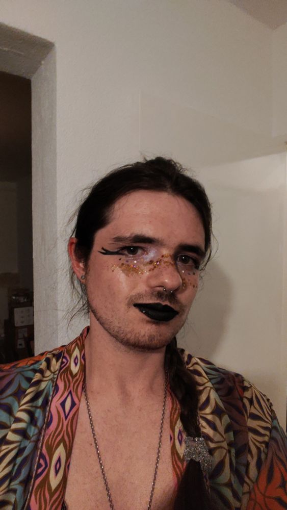 Me wearing colourful makeup and shiny gold glitter with a braid and a lace bra and a patterned flowy top